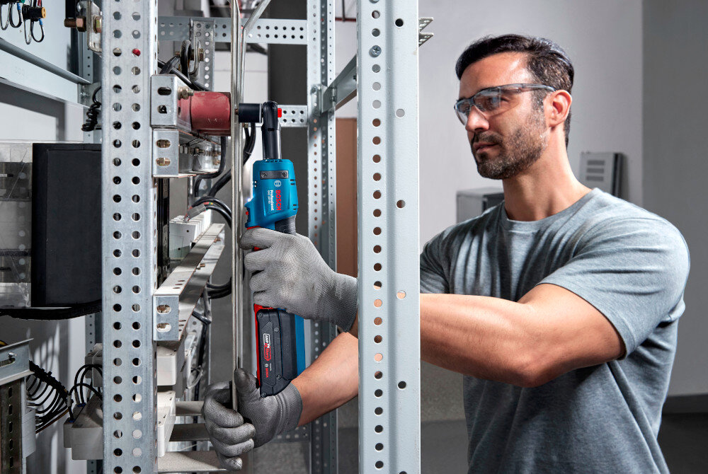 Klucz akumulatorowy grzechotka BOSCH GRC 18V-60 06019N8001 pomieszczenie osoba skręca metalowy stelaż w tle biała ściana system ECP (Electronic Cell Protection) chroni ogniwa przed przegrzaniem i przeciążeniem minimalizuje ryzyko awarii i uszkodzenia baterii