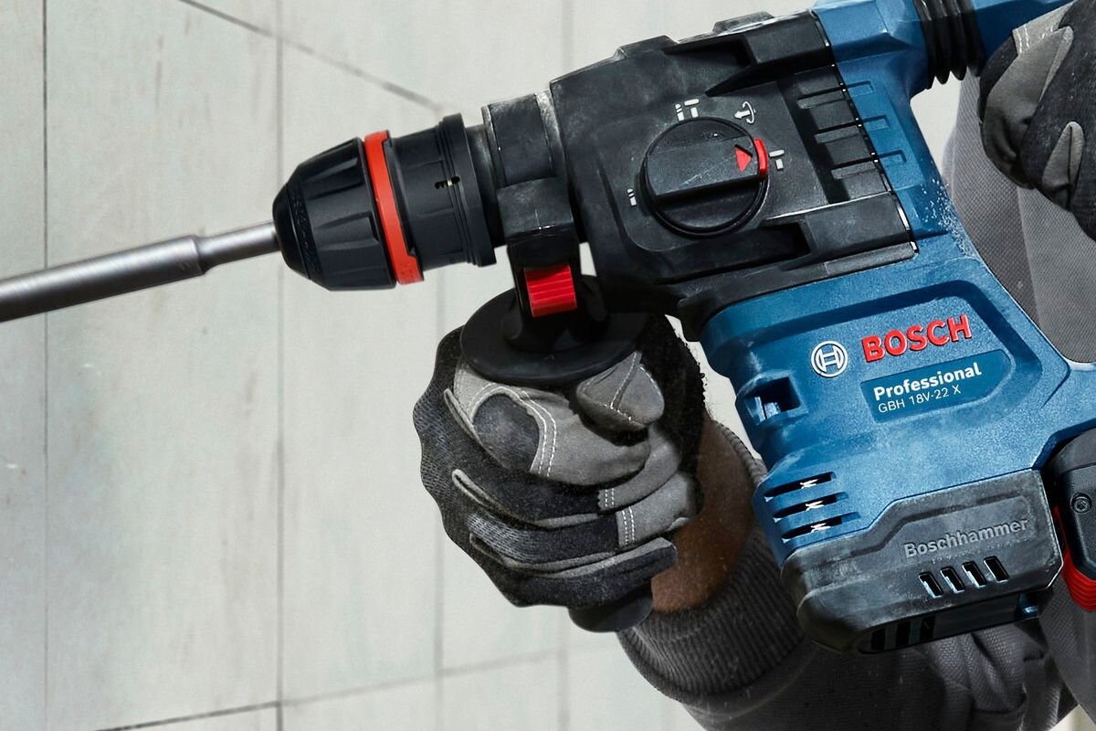 BOSCH GBH 18V-22 X 3,3 kg bez akumulatora ergonomiczny uchwyt cięższymi młotami antypoślizgowa powierzchnia rękojeści - Zbliżenie na dłonie w rękawicach ochronnych trzymające młot udarowo-obrotowy podczas pracy.