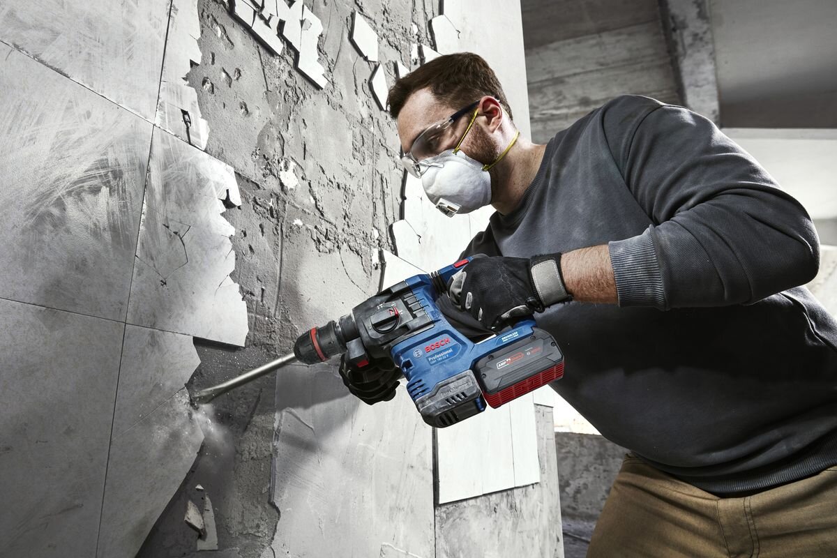 BOSCH GBH 18V-22 X Funkcja udaru nominalnej energii udaru 1,5 J liczbie udarów do 5000 obr/min Prędkość obrotowa bez obciążenia wynosi 0–900 obr/min - Mężczyzna w okularach ochronnych trzyma oburącz pracujący młot udarowo-obrotowegy.