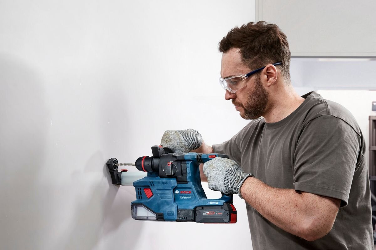 BOSCH GBH 18V-22 X obsługuje wiertła SDS plus 4–22 mm 6–12 mm wiertarkami uniwersalnymi twardymi materiałami - Mężczyzna wierci otwór w ścianie używając młota udarowo-obrotowego