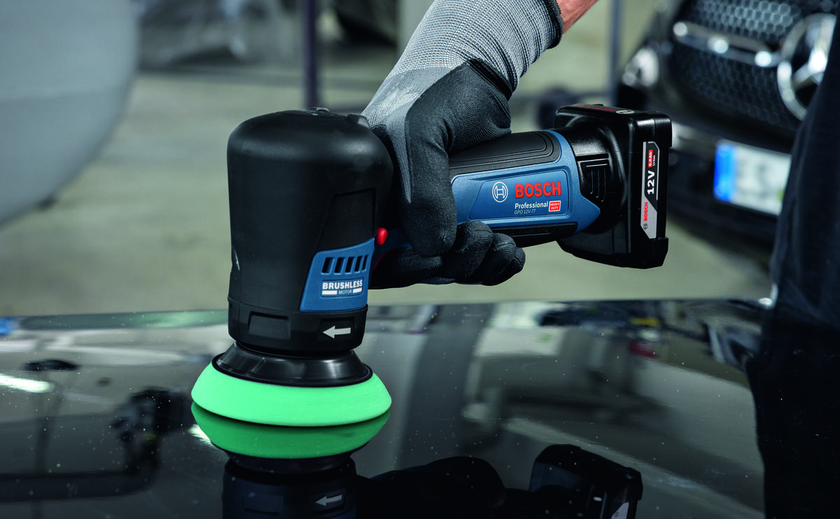 BOSCH Professional GPO 12V-77 06019L3000 Silnik bezszczotkowy BOSCH Professional GPO 12V-77 06019L3000 mniejszym zużyciem elementów standardowy silnik szczotkowy - Zbliżenie na dłonie w rękawicach ochronnych trzymające polerkę akumulatorową Bosch podczas pracy na powierzchni lakierowanej.