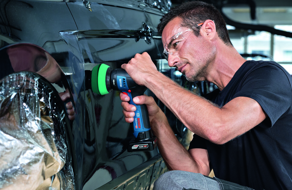 BOSCH Professional GPO 12V-77 06019L3000 Regulacja prędkości obrotowej od 1400 do 7000 obr./min Soft start - Mężczyzna w okularach ochronnych klęczy przy samochodzie i poleruje jego czarną karoserię polerką akumulatorową.