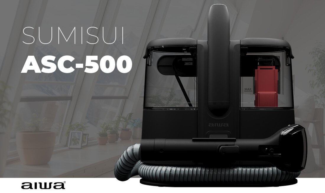 Obraz przedstawia odkurzacz piorący z widocznym napisem \'SUMISUI ASC-500\'. W tle znajdują się duże okna i kilka roślin doniczkowych.