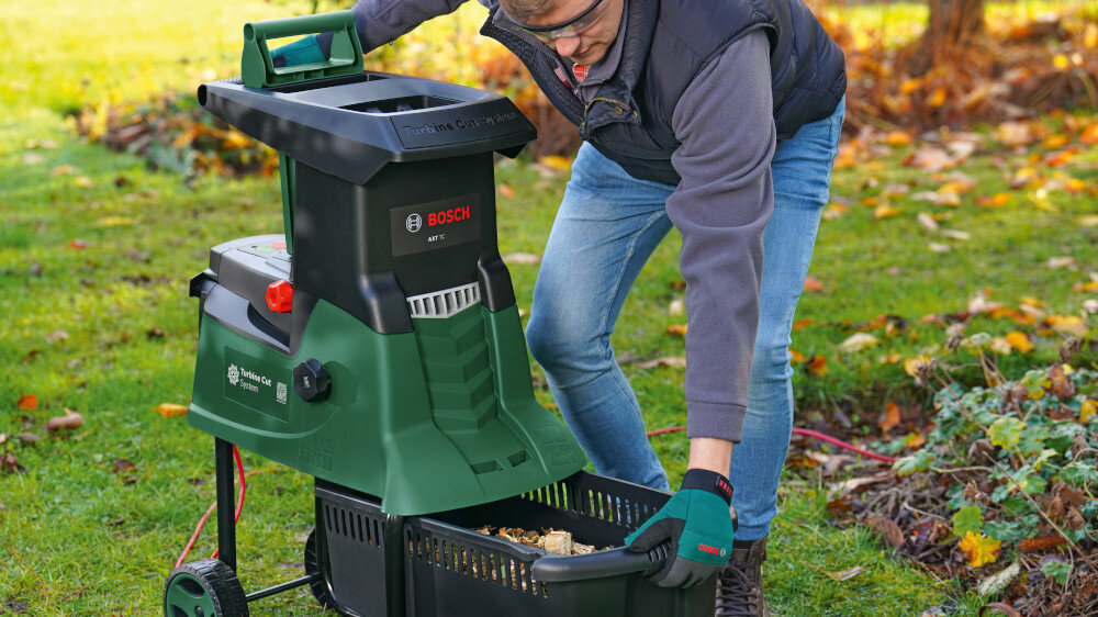 Rozdrabniacz do gałęzi BOSCH AXT 25 TC elektryczny 2500 W sekator + rękawice ogród trawnik osoba wyciąga z rozdrabniacza pojemnik bezpieczeństwo użytkownika stabilna budowa antypoślizgowe elementy przejrzyste zasady obsługi sekator i rękawice w zestawie wygoda i ochrona