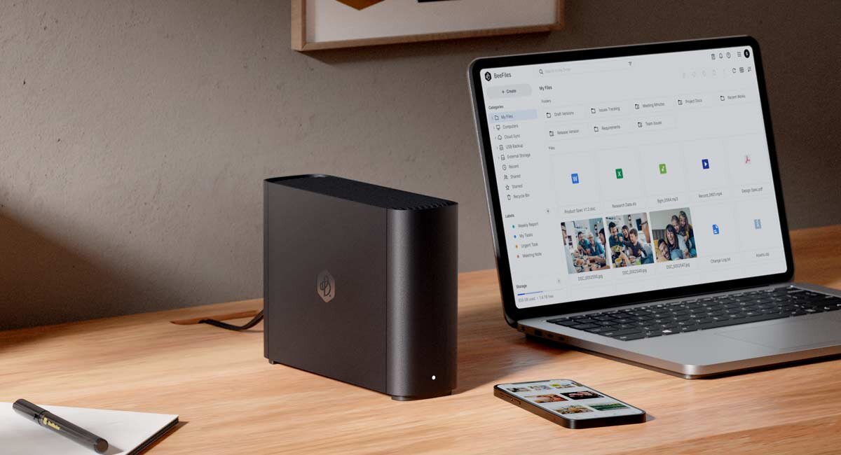 Synology BeeStation Plus BST170-8T obok laptopa na i telefonu na drewnianym biurku.