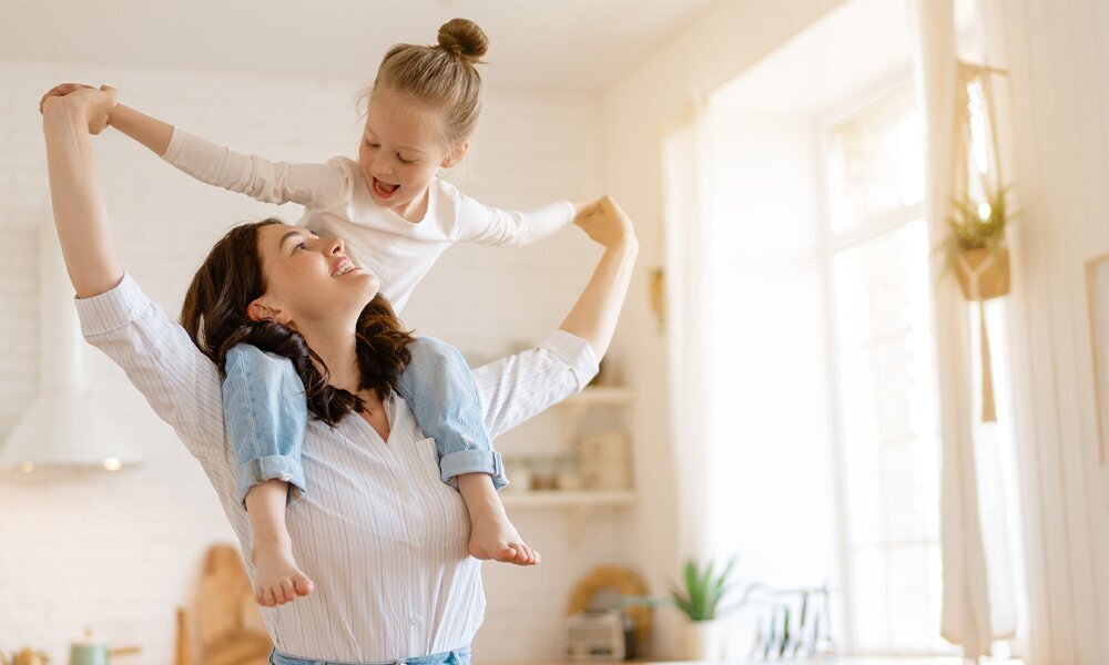 LODÓWKA MIDEA MDRS619FIE45 Kobieta bawi się z dzieckiem, unosząc je na ramionach w jasnej kuchni. Scena oddaje radość wspólnie spędzanego czasu alarm otwartych drzwi ochrona żywność energia panel LED Multi Air Flow kompresor inwerterowy Fast Cooling