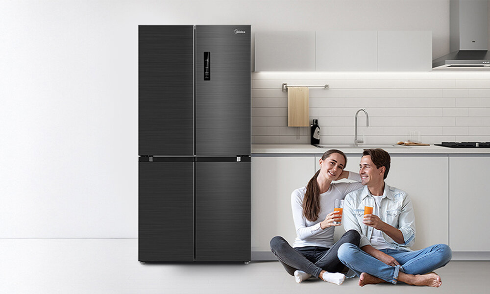 LODÓWKA MIDEA MDRF632FIE45 Dwie osoby siedzą na podłodze w kuchni i trzymają napoje, a obok nich stoi ciemna lodówka. Całość tworzy spokojną, domową scenę