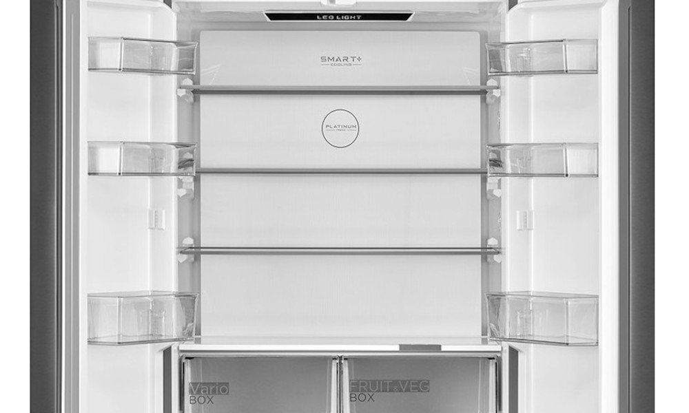 Wnętrze lodówki z kilkoma półkami i szufladami, na górze widoczny napis \'LED LIGHT\'. Na drzwiach znajdują się przezroczyste pojemniki, a na jednej z półek napis \'SMART+\' oraz \'PLATINUM\'.