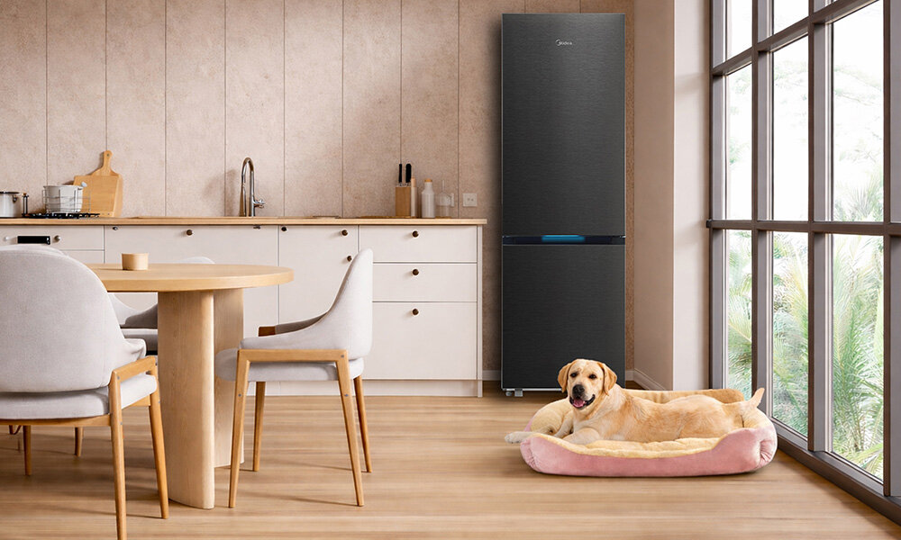 LODÓWKA MIDEA MDRB548MIC45P Lodówka stoi w kuchni obok okna, a na podłodze leży pies w wygodnym legowisku. Jasna przestrzeń sprawia, że cała scena wygląda przytulnie ciemne wykończenie design funkcjonalność technologia pojemność