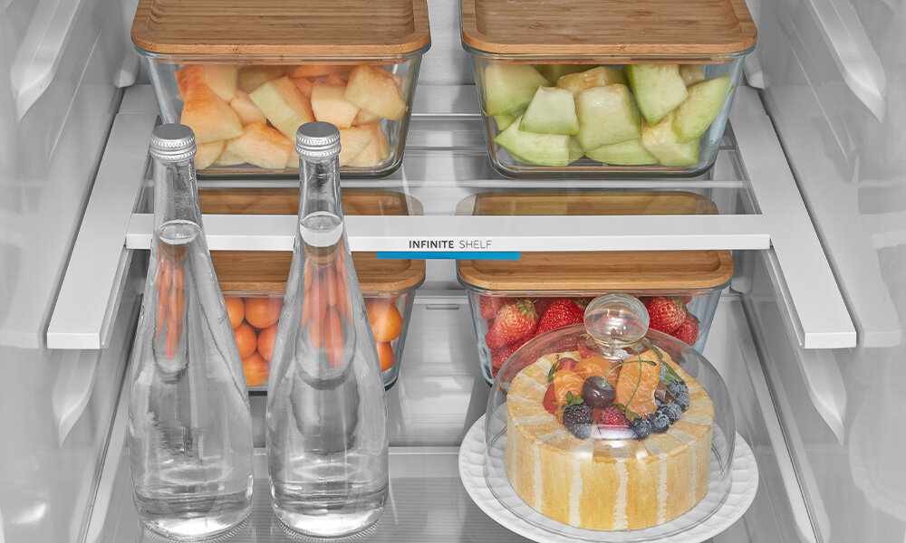 LODÓWKA MIDEA MDRB548MIC45P W lodówce ustawione są szklane pojemniki z owocami oraz butelki wody, uporządkowane na szklanych półkach oraz widoczna półka INFINITE SHELF (nieskończona). Na dole widoczny jest deser pod szklaną pokrywą regulowane półki nieskończona półka półki drzwiowe szuflady zamrażarki