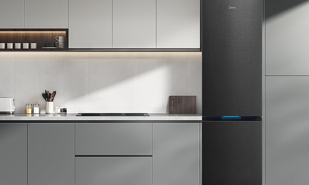 LODÓWKA MIDEA MDRB600MIC45P Lodówka stoi przy kuchennej zabudowie w prostym, jasnym wnętrzu. Całość jest schludna, z widocznymi drobnymi akcesoriami kuchennymi na blacie