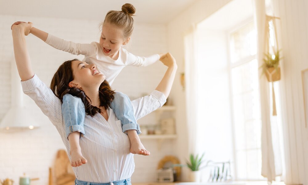 LODÓWKA MIDEA MDRB600MIC45P W kuchni kobieta unosi dziecko na ramionach, tworząc pełną energii scenę. Pomieszczenie jest jasne i wypełnione naturalnym światłem panel LED Super Cool Super Freeze Vacation Smart Home