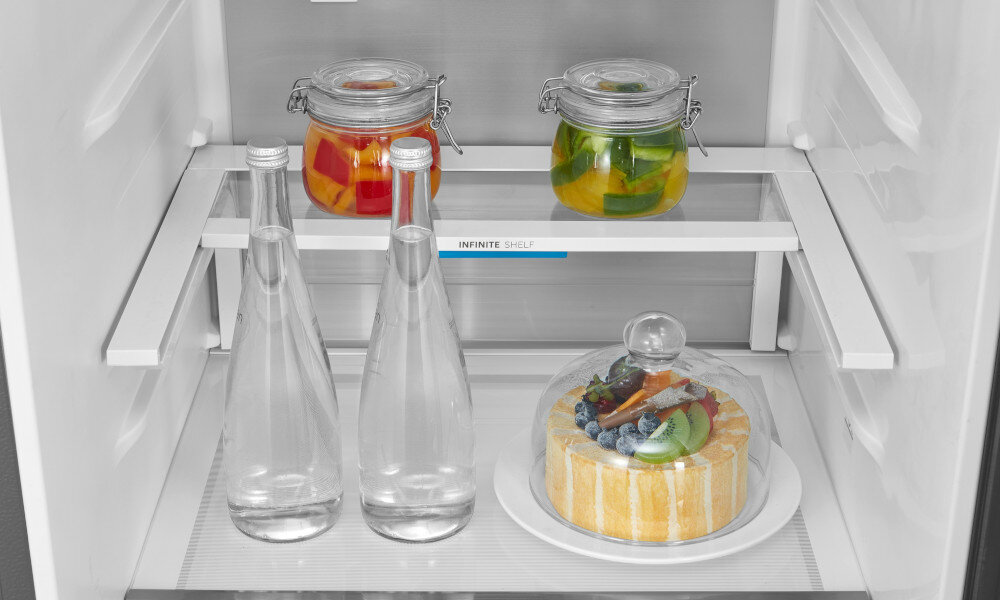 LODÓWKA MIDEA MDRB600MIC45P W lodówce ustawiono słoiki z warzywami, butelki z wodą oraz deser na talerzu. Wszystkie elementy rozmieszczono na szklanych półkach, umożliwiając wygodny dostęp Infinite Shelf elastyczne wnętrze przesuwne półki pojemniki
