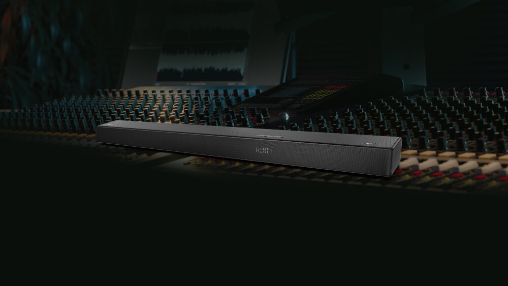 Na obrazie widoczny jest czarny soundbar z napisem \'HISENSE\' na tle panelu sterowania z wieloma przyciskami i suwakami. Tło jest ciemne, co podkreśla nowoczesny design urządzenia.