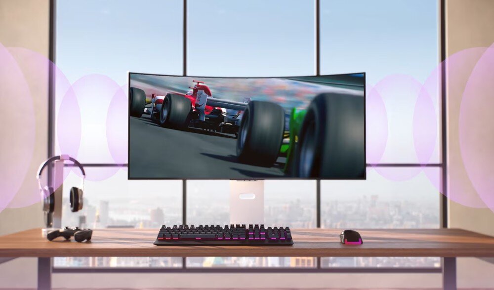 Monitor LG UltraGear 39GX90SA-W.AEU Na biurku znajduje się zakrzywiony monitor wyświetlający wyścig samochodowy, obok którego leżą słuchawki, klawiatura i myszka. W tle widać duże okno z widokiem na miasto, głośniki, dźwięk