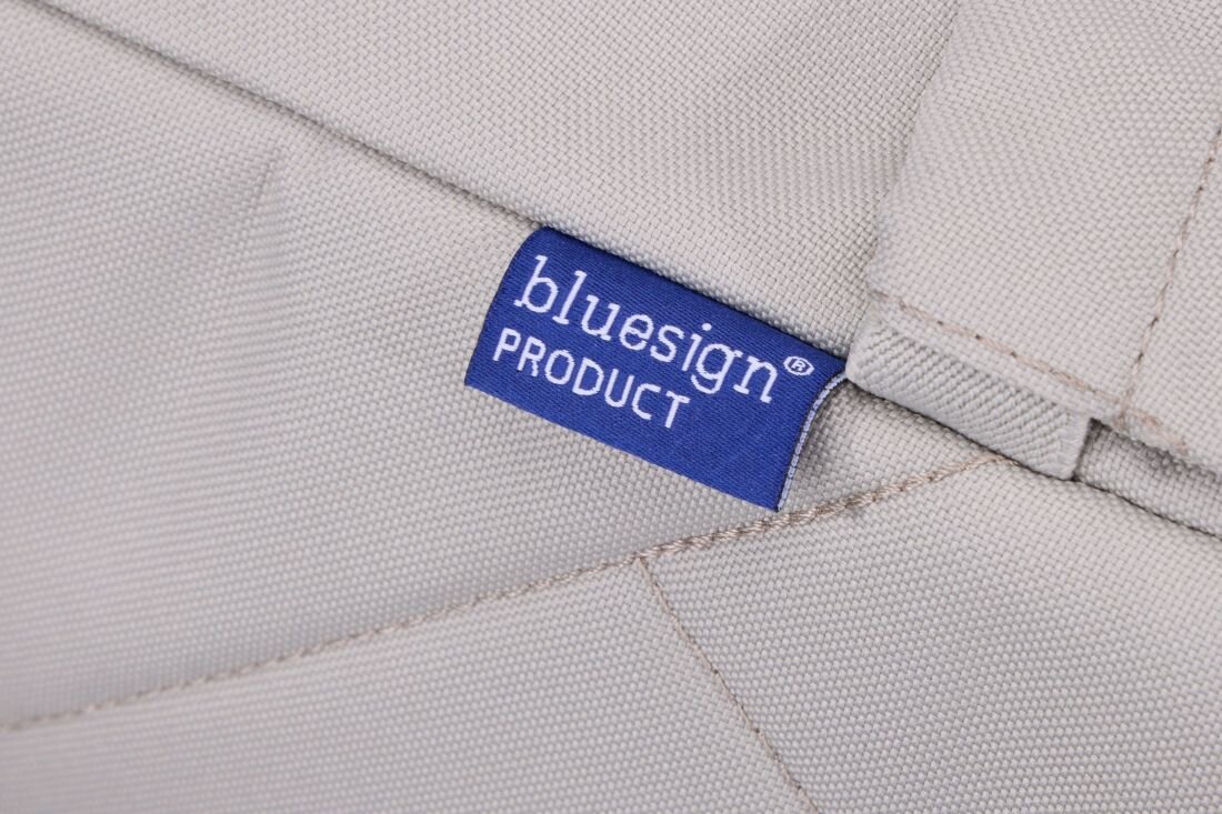Na jasnobeżowym materiale znajduje się niebieska metka z białym napisem \'bluesign PRODUCT\'.