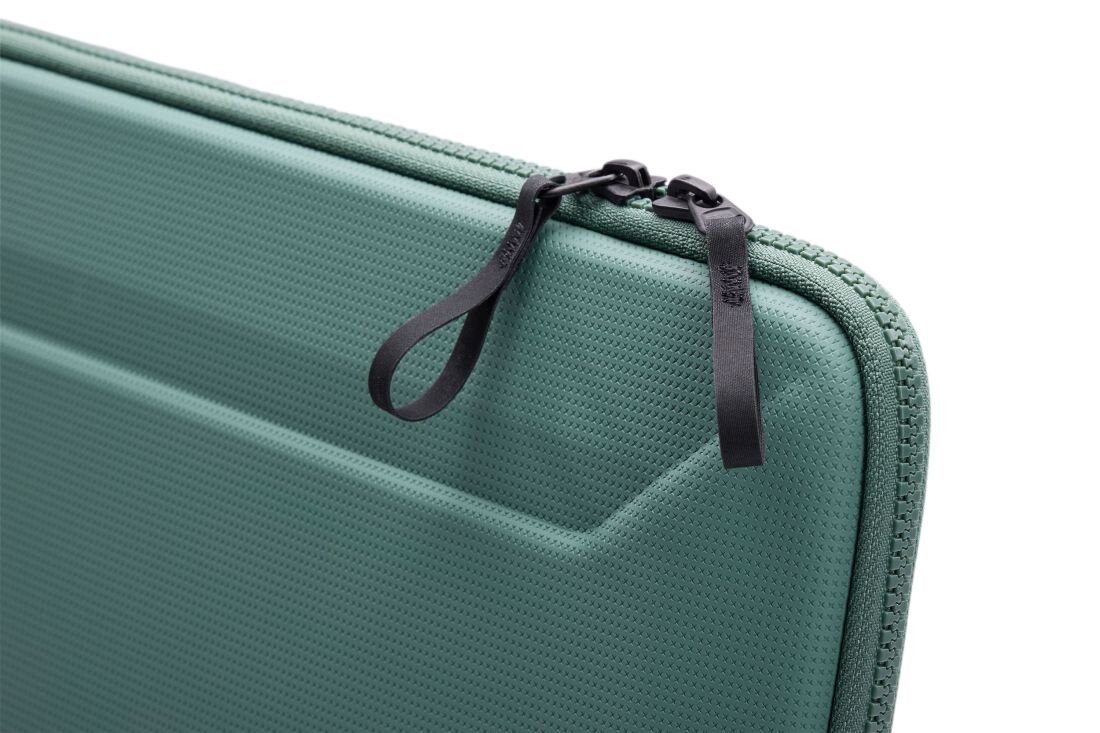 Zielone etui na laptopa z widocznym zamkiem błyskawicznym i dwoma czarnymi uchwytami. Powierzchnia etui ma teksturę z drobnymi wypustkami.