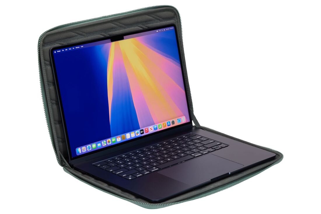 Na obrazie widoczny jest otwarty laptop umieszczony w zielonym etui. Ekran laptopa wyświetla kolorowy gradient, a etui ma pikowaną strukturę wewnętrzną.
