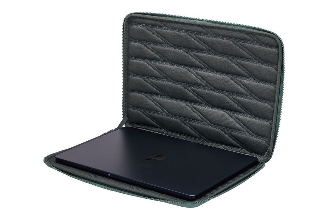 Otwarty zielony pokrowiec na laptopa z widocznym wnętrzem o pikowanej strukturze, w którym znajduje się ciemny laptop. Pokrowiec ma zamek błyskawiczny wzdłuż krawędzi.