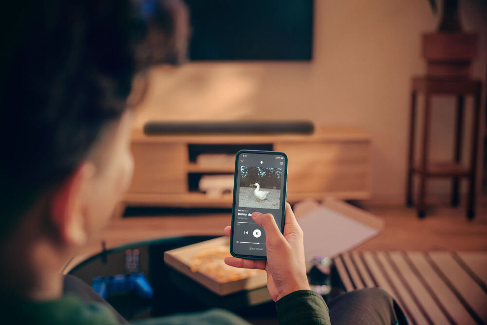 Soundbar JBL BAR 500 MkII PureVoice 2.0 wyraźne dialogi subtelne dźwięki, osoba siedząca na kanapie z telefonem w ręku