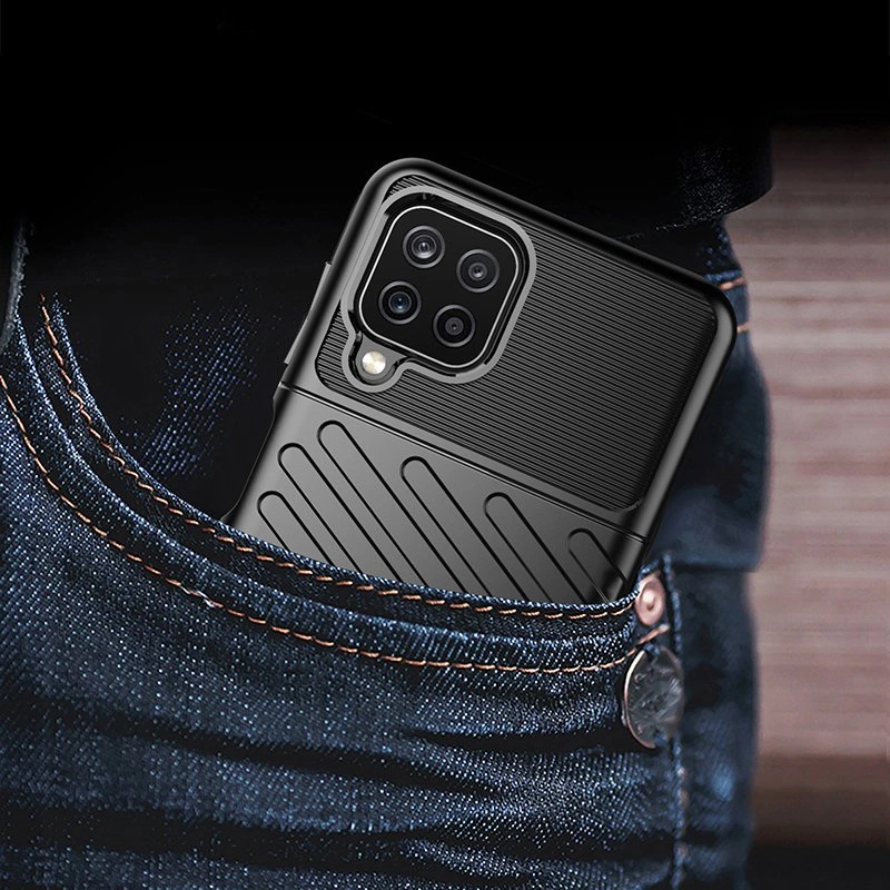 Telefon w czarnym etui z widocznymi czterema obiektywami aparatu wystaje z kieszeni dżinsów. Etui ma teksturowaną powierzchnię z poziomymi i ukośnymi liniami.