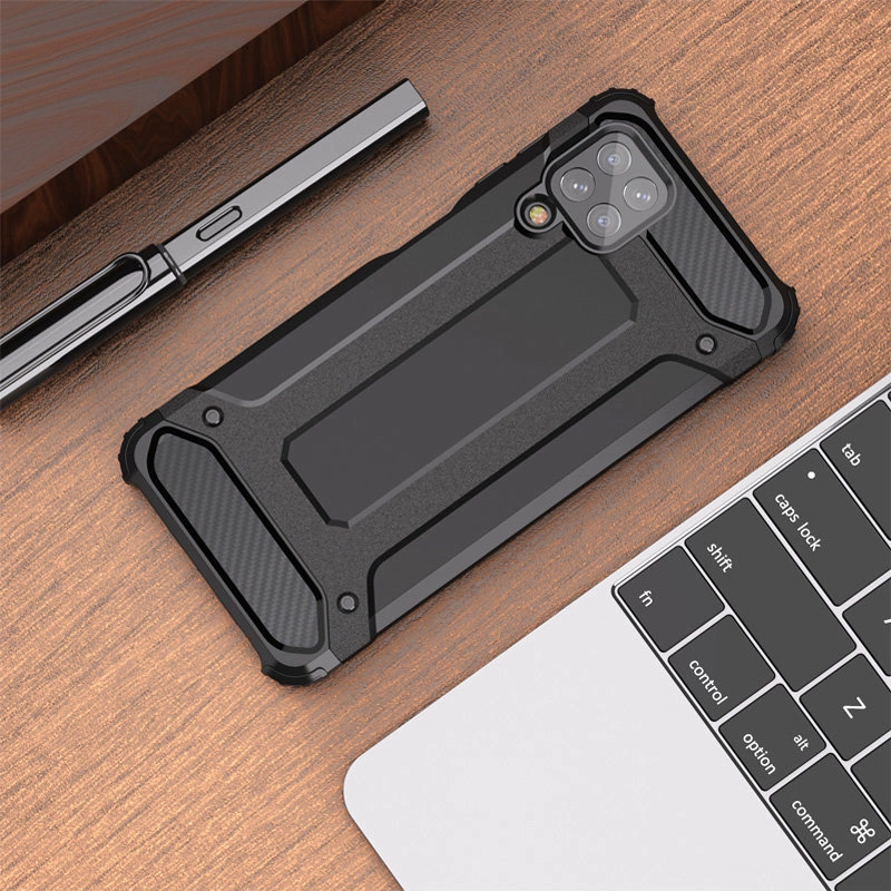 Na drewnianym blacie leży czarne, pancerne etui na telefon z widocznymi wzmocnieniami i wycięciem na aparat. Obok znajduje się srebrny długopis i fragment klawiatury laptopa.