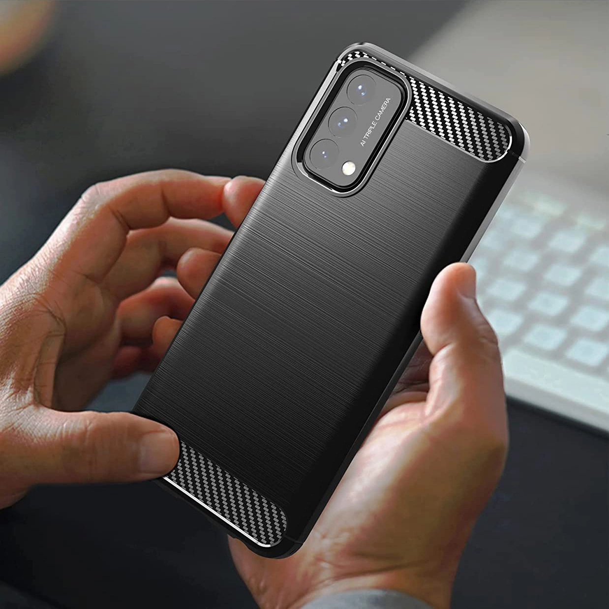 Osoba trzyma czarne etui na telefon z teksturą przypominającą włókno węglowe. Na etui widoczny jest napis \'AI TRIPLE CAMERA\'.