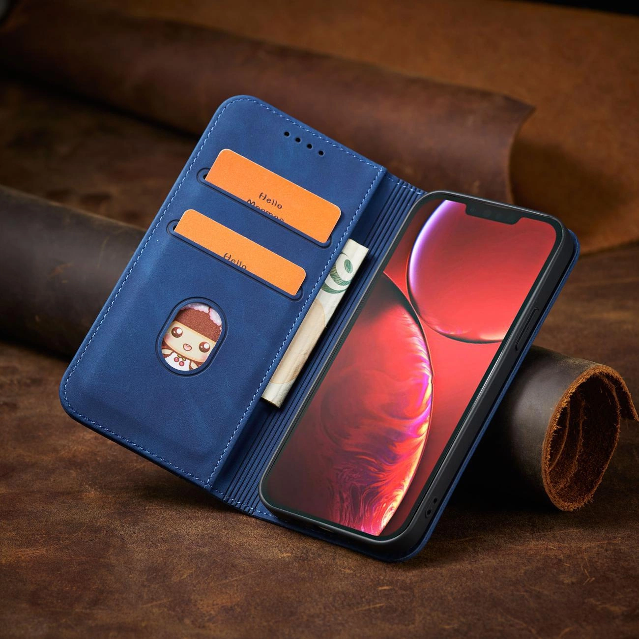 Niebieskie etui na telefon z klapką, posiada dwa miejsca na karty z napisem \'Hello\' oraz kieszeń na banknoty. Obok znajduje się telefon z wyświetlaczem w kolorze czerwonym.