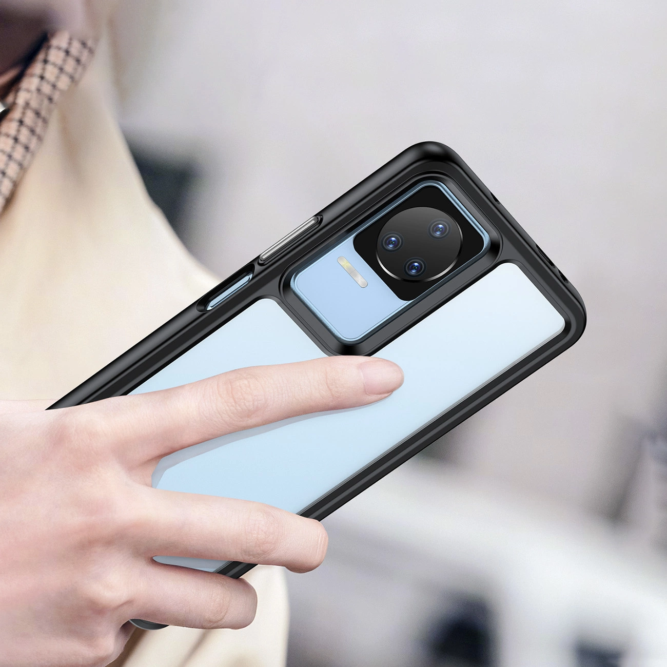 Osoba trzyma telefon w niebieskim etui z elastyczną ramką, widoczny jest moduł aparatu z trzema obiektywami.