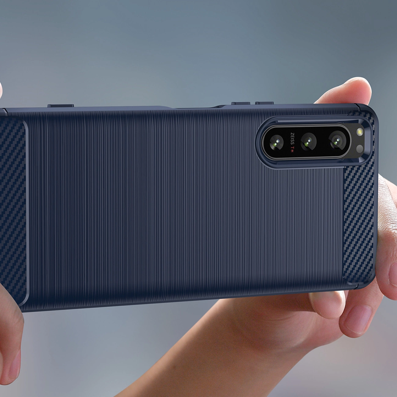 Osoba trzyma telefon w ciemnym, teksturowanym etui z widocznymi trzema obiektywami aparatu i napisem \'ZEISS\'.