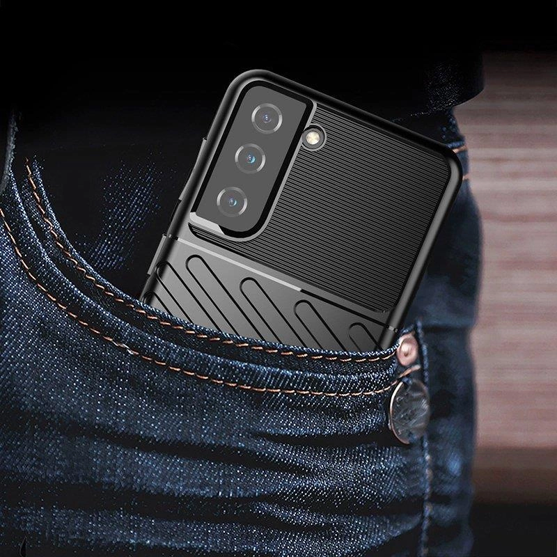 Czarny telefon w etui znajduje się w kieszeni dżinsów. Etui ma teksturowaną powierzchnię i wycięcia na aparat oraz lampę błyskową.