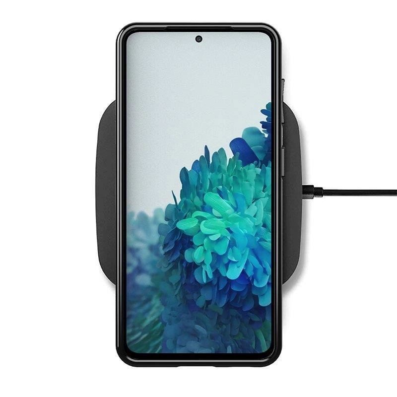 Na obrazie widoczny jest smartfon z wyświetlaczem przedstawiającym niebiesko-zielone abstrakcyjne wzory, umieszczony na ładowarce bezprzewodowej. Telefon jest w czarnym etui, a do ładowarki podłączony jest kabel.
