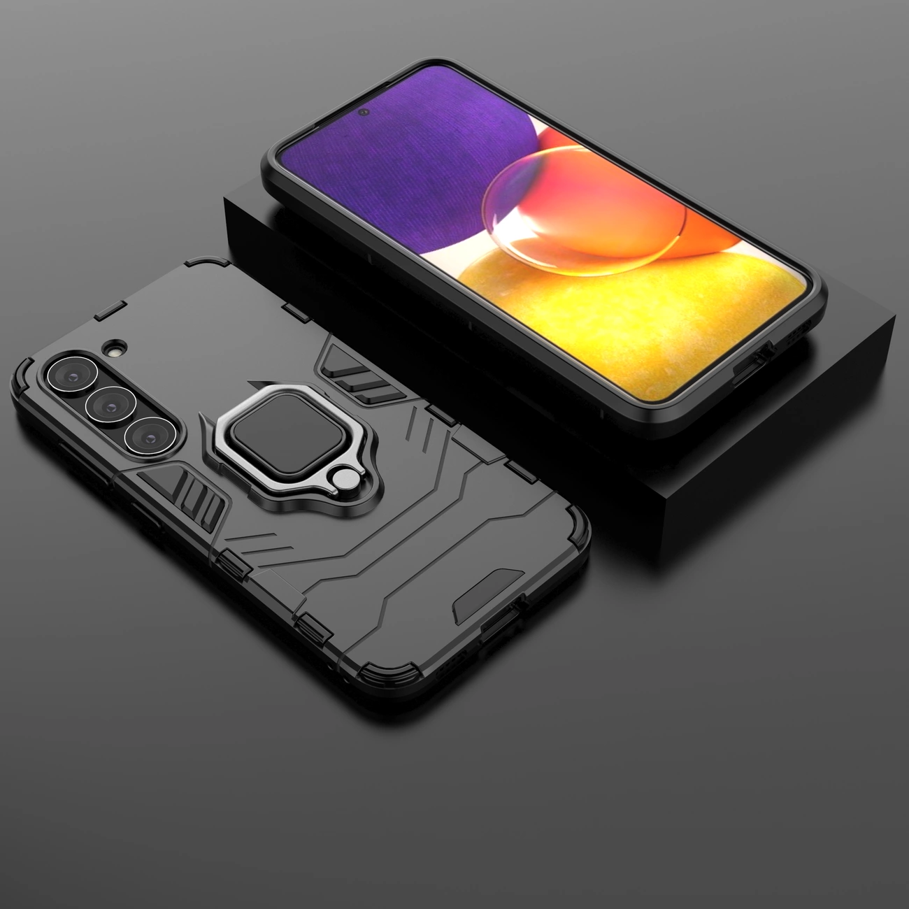 Na obrazie widoczne jest czarne etui ochronne z uchwytem magnetycznym, przeznaczone do telefonu Samsung Galaxy S23. Obok etui znajduje się telefon z wyświetlaczem pokazującym kolorowy obraz.