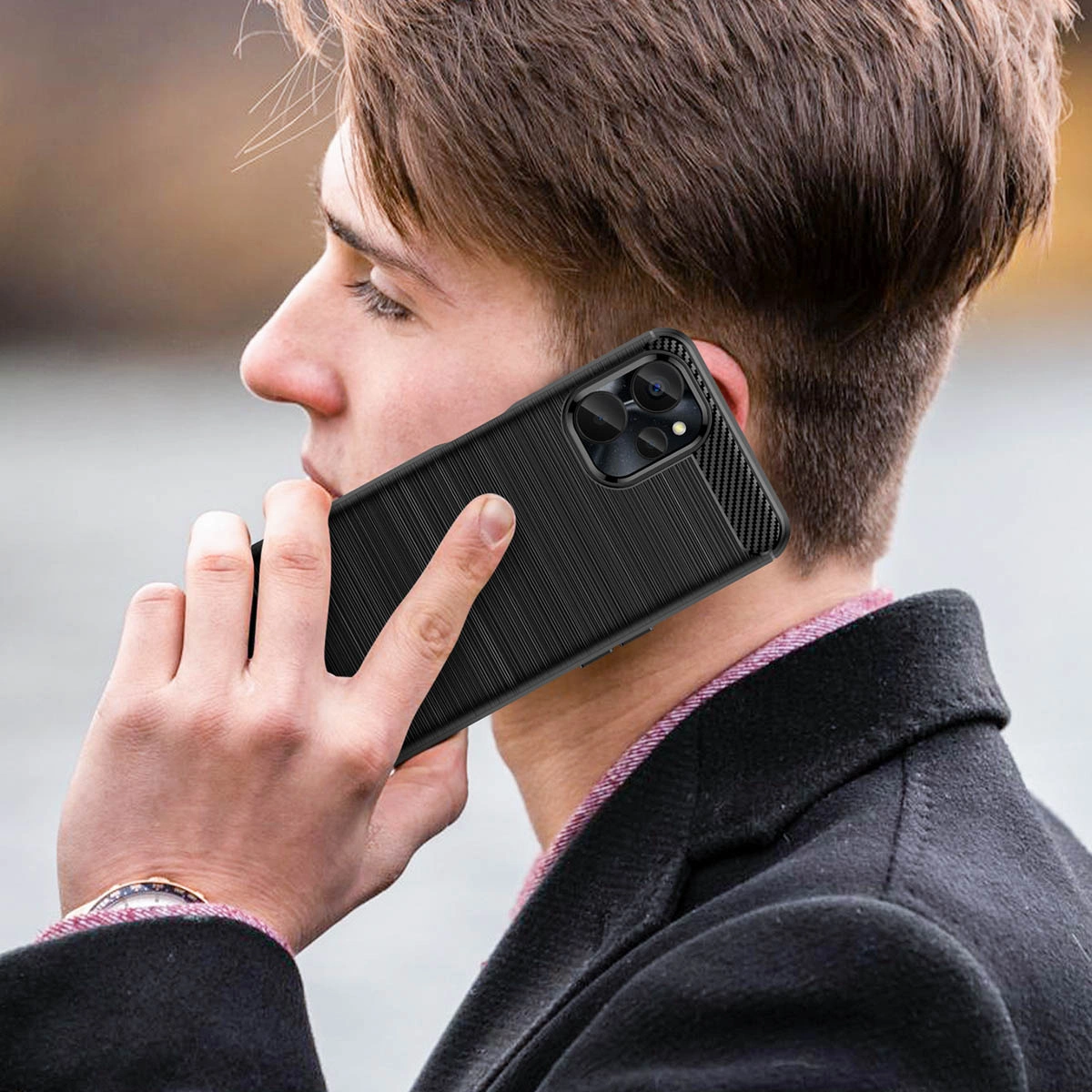 Osoba trzyma przy uchu telefon w czarnym, karbonowym etui z widocznymi wycięciami na aparat. Tło jest rozmyte, co podkreśla główny obiekt zdjęcia.