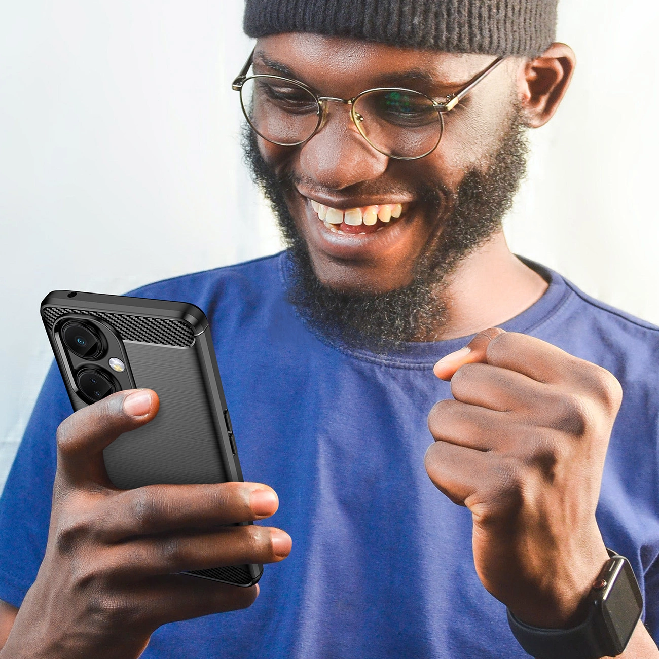 Osoba trzyma smartfon w czarnym, karbonowym etui, uśmiechając się i patrząc na ekran. Etui ma teksturę przypominającą włókno węglowe i wycięcia na aparaty.