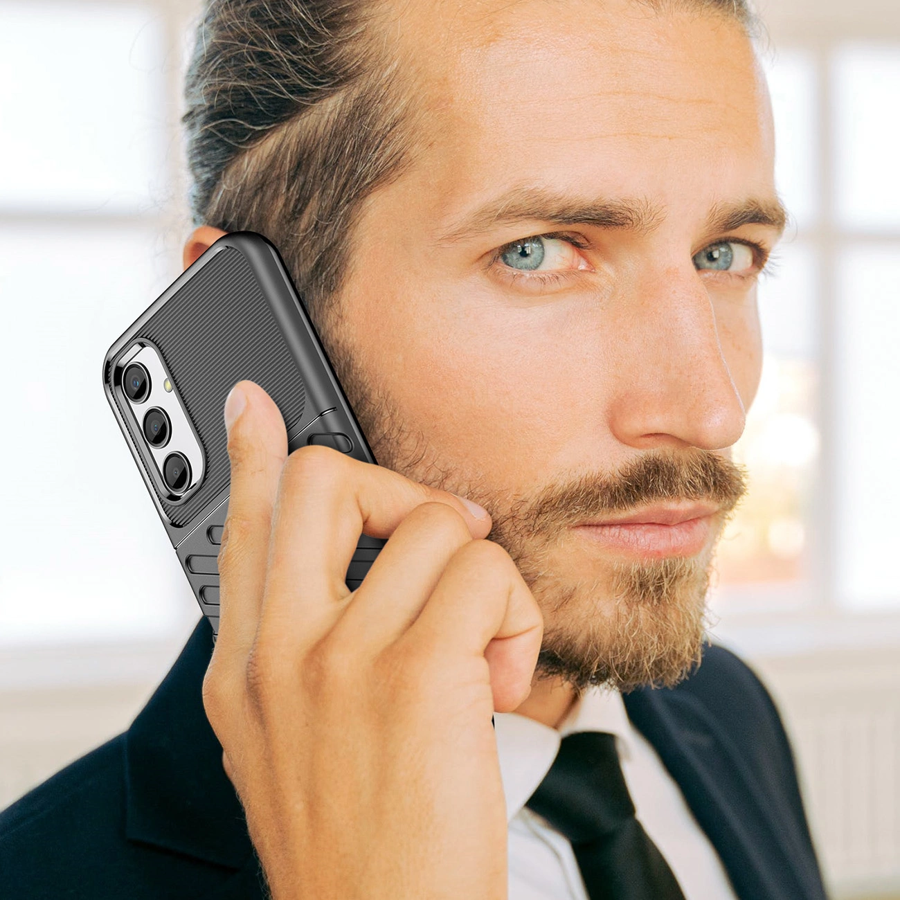 Osoba trzyma telefon z czarnym, pancernym etui przy uchu. Etui ma wyraźne tekstury i otwory na trzy obiektywy aparatu.