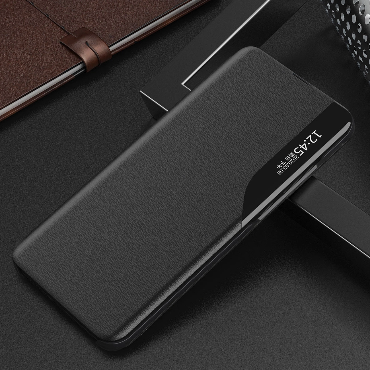 Czarne etui na telefon z klapką, wykonane z materiału przypominającego skórę, leży na ciemnej powierzchni. Na etui widoczny jest wyświetlacz z godziną 12:45 i datą 2020.08.08.