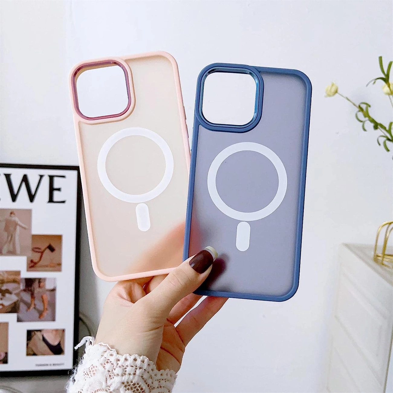 Na zdjęciu widoczne są dwa etui na telefon, jedno w kolorze różowym, a drugie w fioletowym, oba z białym okręgiem na środku. W tle znajduje się plakat z napisem \'WE\'.