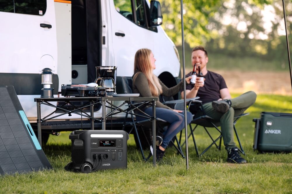 Stacja zasilania ANKER Solix F2600 2560 Wh 2300W, zasilanie, moc, prąd, energia, ładowanie, stacja, para siedzi przy kamperze, na pierwszym planie stacja zasilania na ziemi