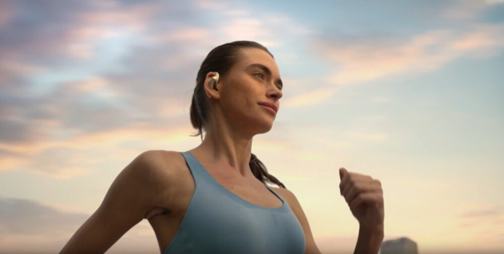 Słuchawki SHOKZ OpenFit 2 otwarta konstrukcja komfort noszenia dźwięk przestrzenny, osoba siedzaca przed komputerem w słuchawkach