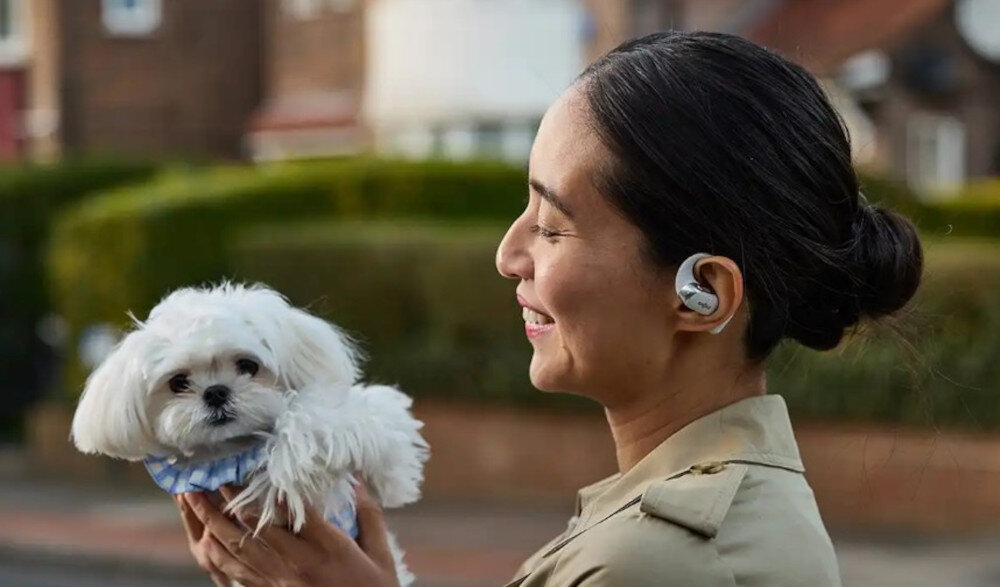 Słuchawki SHOKZ OpenFit 2+ otwarta konstrukcja komfort Ultra-Soft Silicone 2.0, osoba z założonymi słuchawkami z psem na rękach