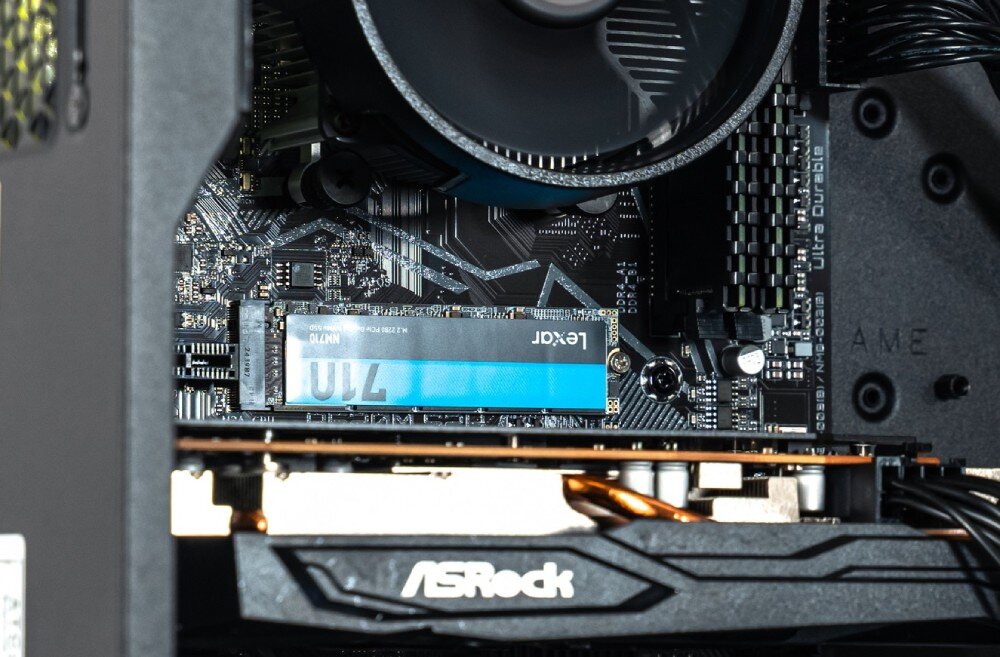 Komputer OPTIMUS E-Sport GA520T-CR9 Zbliżenie na podzespoły zamontowane na płycie głównej, w tym okrągłe chłodzenie procesora, dwa moduły pamięci RAM oraz dysk SSD M.2 z zieloną naklejką, pamięć RAM, taktowanie, dysk, pojemność