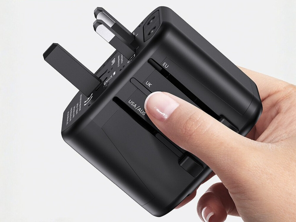 Adapter podróżny USAMS T55 US-CC173 ładowarka USB 2 porty LED Zbliżenie na dłoń operującą suwakami bocznego panelu adaptera USAMS, wysuwającymi wtyczki standardu UK oraz USA/AUS.