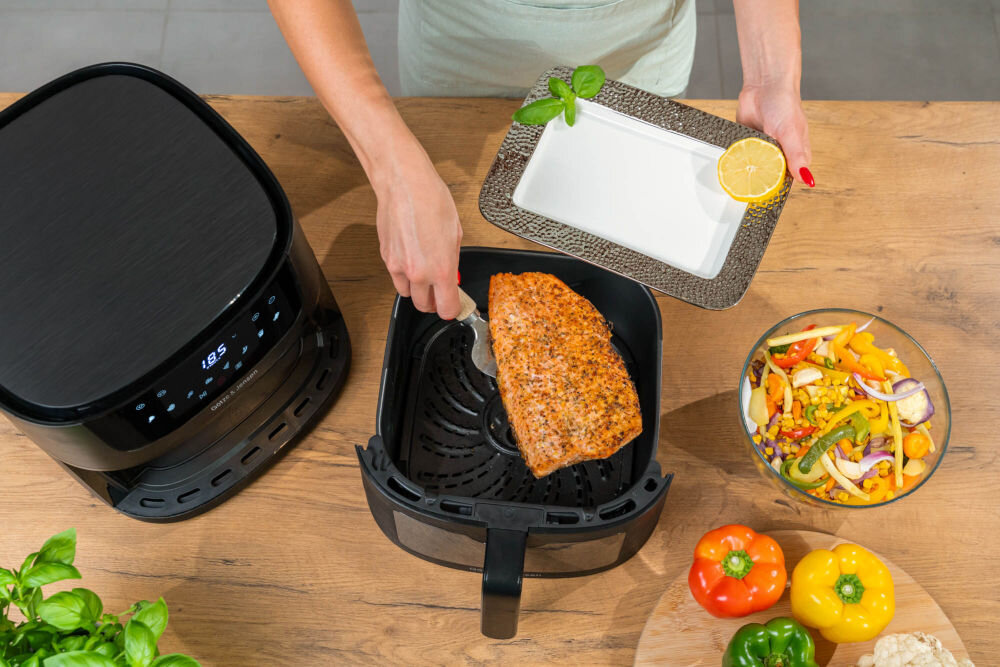 Frytkownica beztłuszczowa GÖTZE & JENSEN AF610K technologia Air Fry do zdrowego gotowania bez oleju chrupiące frytki warzywa nuggetsy Widok z góry na frytkownicę Götze & Jensen i wyjmowanie upieczonego fileta z łososia z kosza urządzenia.