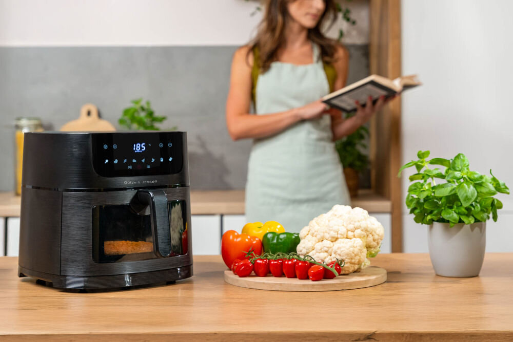 Frytkownica beztłuszczowa GÖTZE & JENSEN AF610K 1500 W szybsze gotowanie niż piekarnik oszczędność energii Czarny Air Fryer Götze & Jensen w kuchni z wyświetlaczem wskazującym 185 stopni Celsjusza i okienkiem podglądu potrawy.
