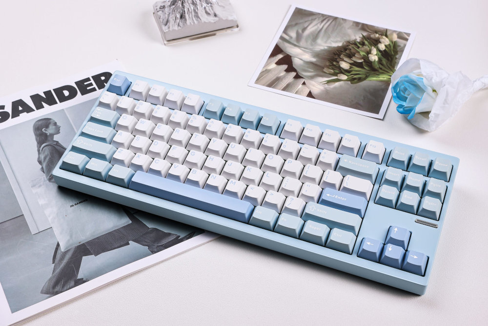 MCHOSE GX87 mechaniczna klawiatura Obudowa z aluminium CNC 150-mesh surfacing Przełączniki Matcha Latte - klawiatura w niebieskim odcieniu położona na zdjęciach