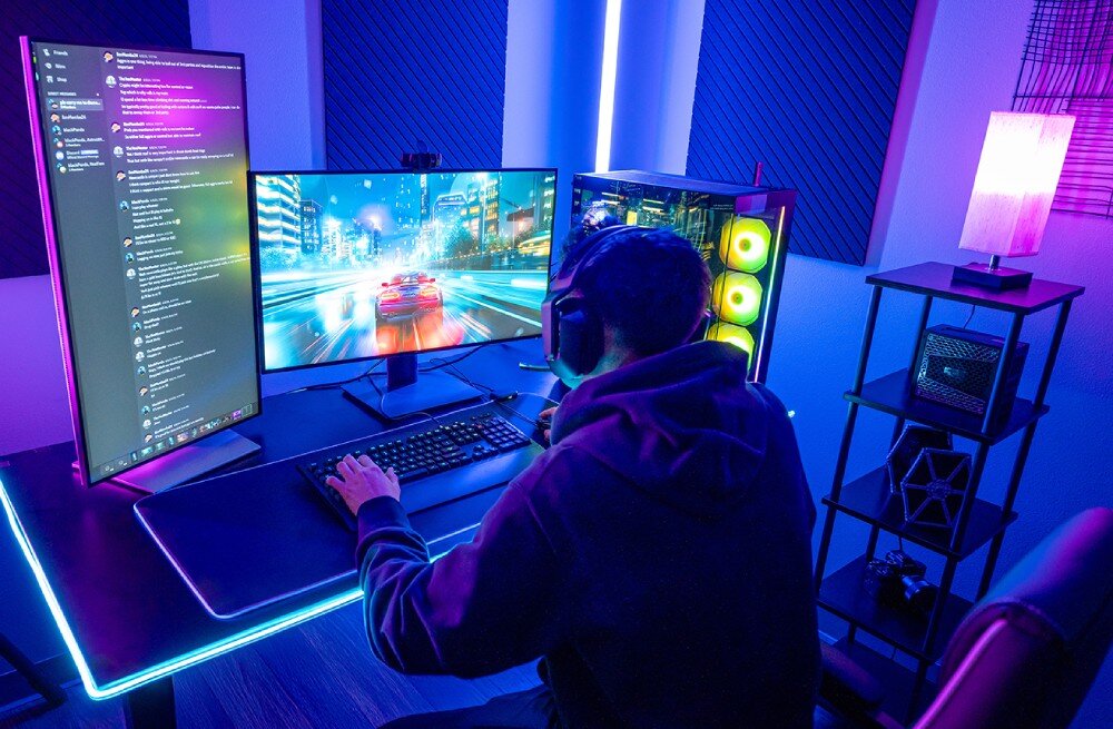 Dysk CRUCIAL T710 Osoba grająca przy biurku z dwoma monitorami, z których jeden jest ustawiony pionowo, a drugi wyświetla grę wyścigową, w tle obudowa komputera z podświetleniem wentylatorów, technologia, prędkość, wydajność