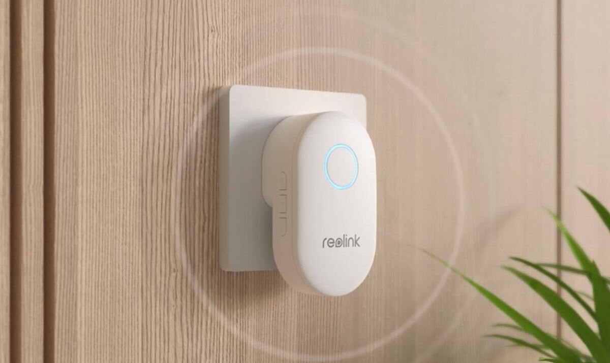 Wideodzwonek REOLINK D340W Bezprzewodowy Wi-Fi Biały, rozmowa, powiadomienie, integracje, nagrania, Chime (dzwonek) Reolink podłączony do gniazdka w jasnym drewnianym pomieszczeniu, widoczne światło LED.