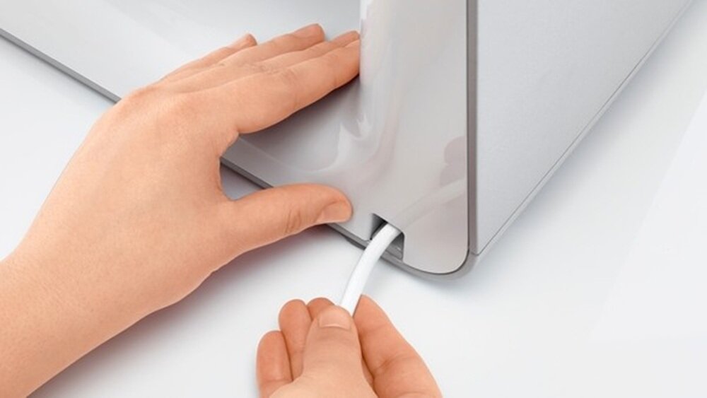 Dwie ręce trzymają biały kabel, który jest wkładany do gniazda w szarej obudowie urządzenia.