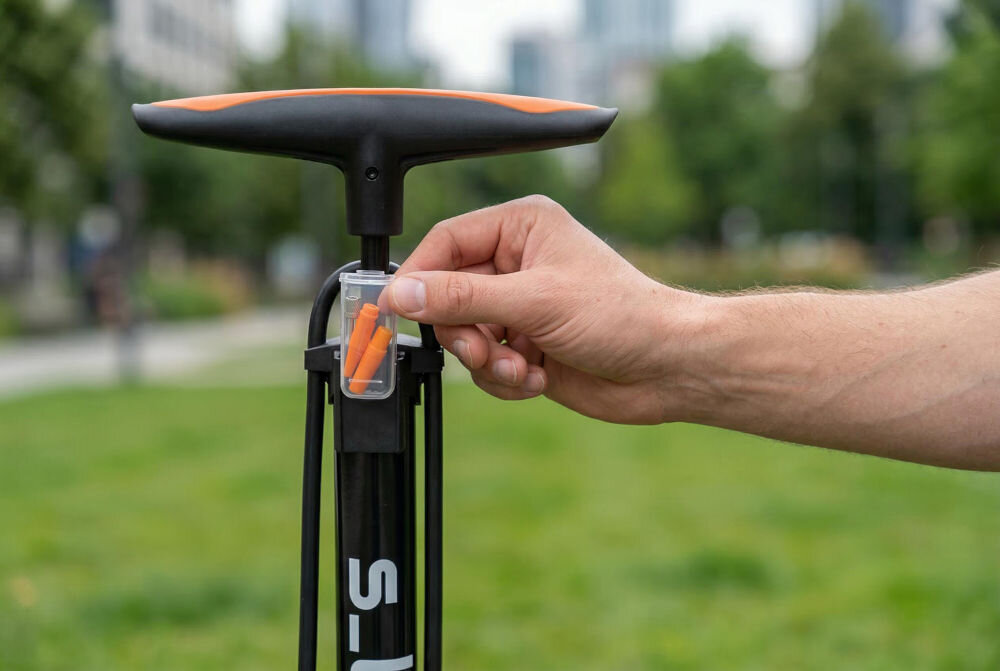 Pompka rowerowa S-LINE VPO403 Mężczyzna pompuje koło czarnego roweru trekkingowego za pomocą pompki podłogowej S-LINE. Zdjęcie w plenerze pokazuje wygodną pozycję podczas pracy dzięki stabilnej podstawie urządzenia i długiemu elastycznemu wężykowi.